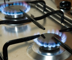 The image features a close-up of a gas stovetop with blue flames emanating from two burner rings. The burners are circular, made of metal, and are installed on a silver stainless steel surface. The flames are vibrant and create a warm glow, indicating that the burners are ignited and ready for cooking.